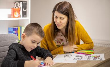 Une femme regarde un jeune garçon en train de faire un dessin