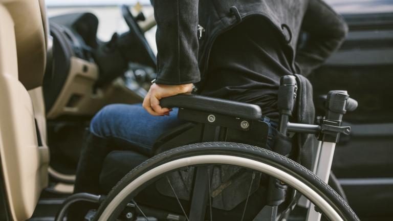 Un homme dans un fauteuil roulant s'apprête à s'installer au volant d'une voiture